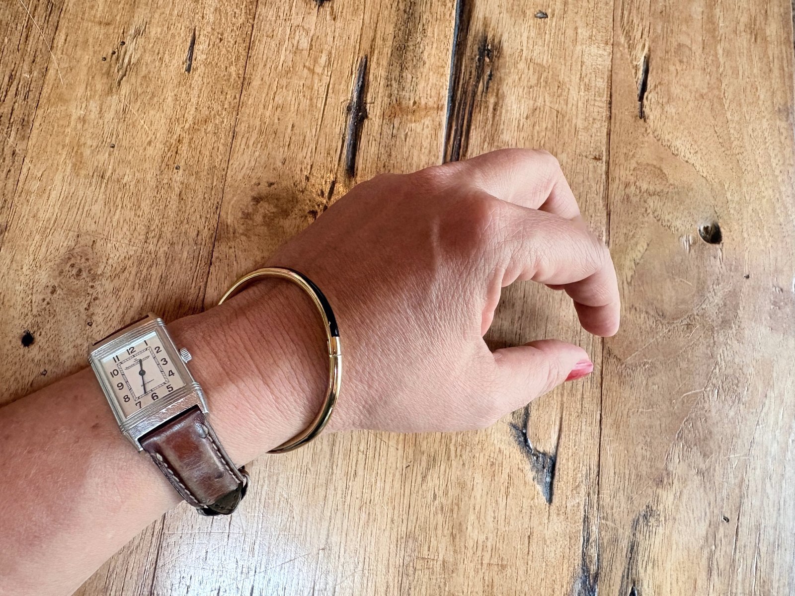 Poignet de Valérie, montre Reverso et jonc doré, posé sur une table en bois ancien