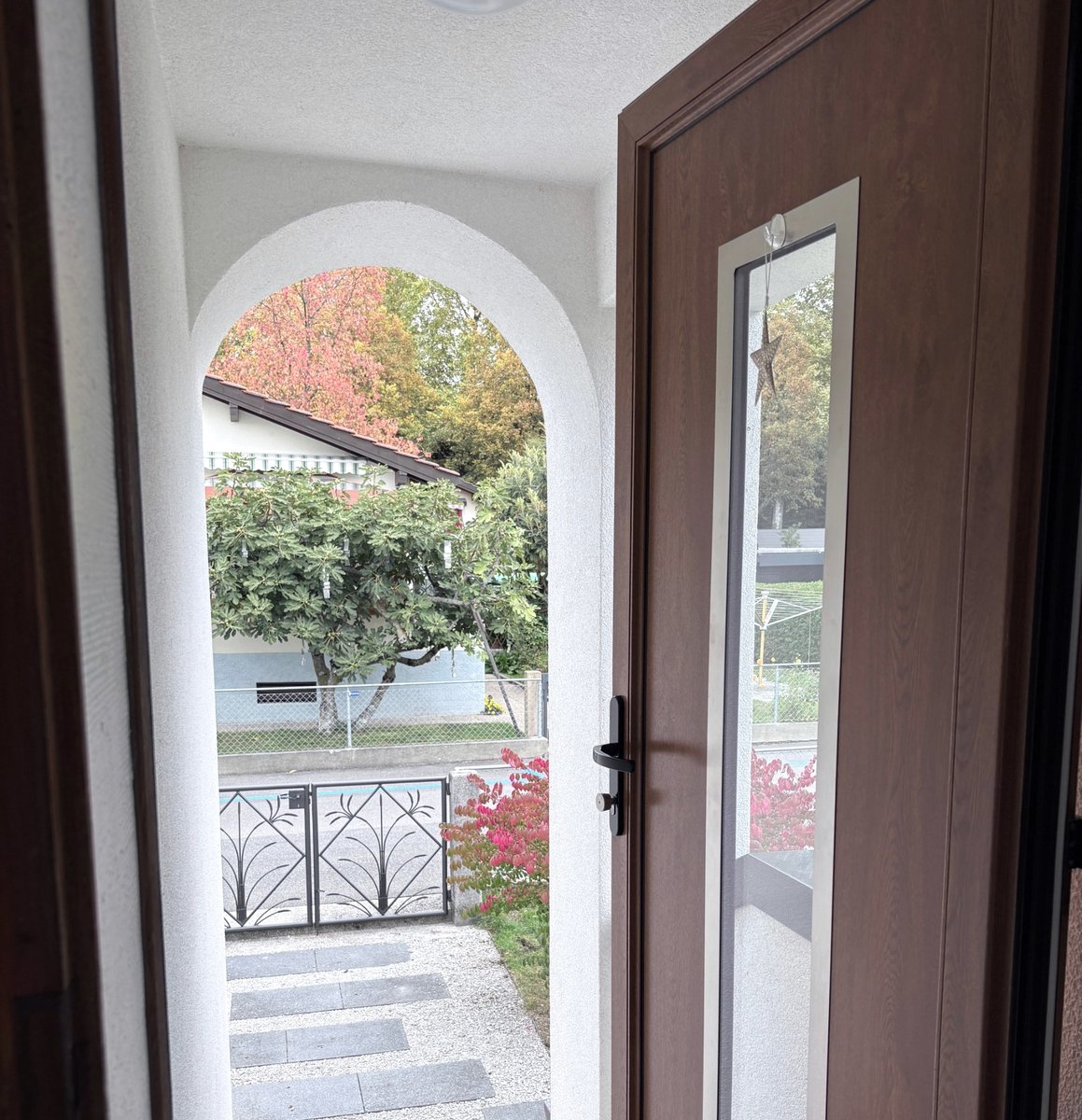 La porte d’entrée ouverte sur l’arche blanche, le chemin de dalles et le portail en fer forgé